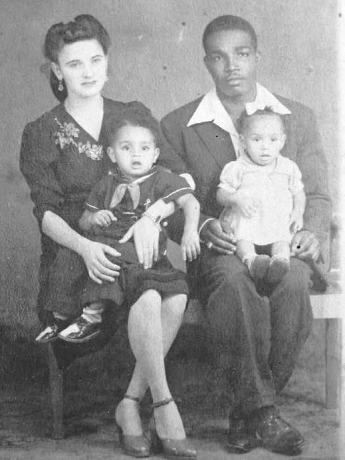 Black and white antique historical photograph of a family of four seated together, dressed in vintage clothing.