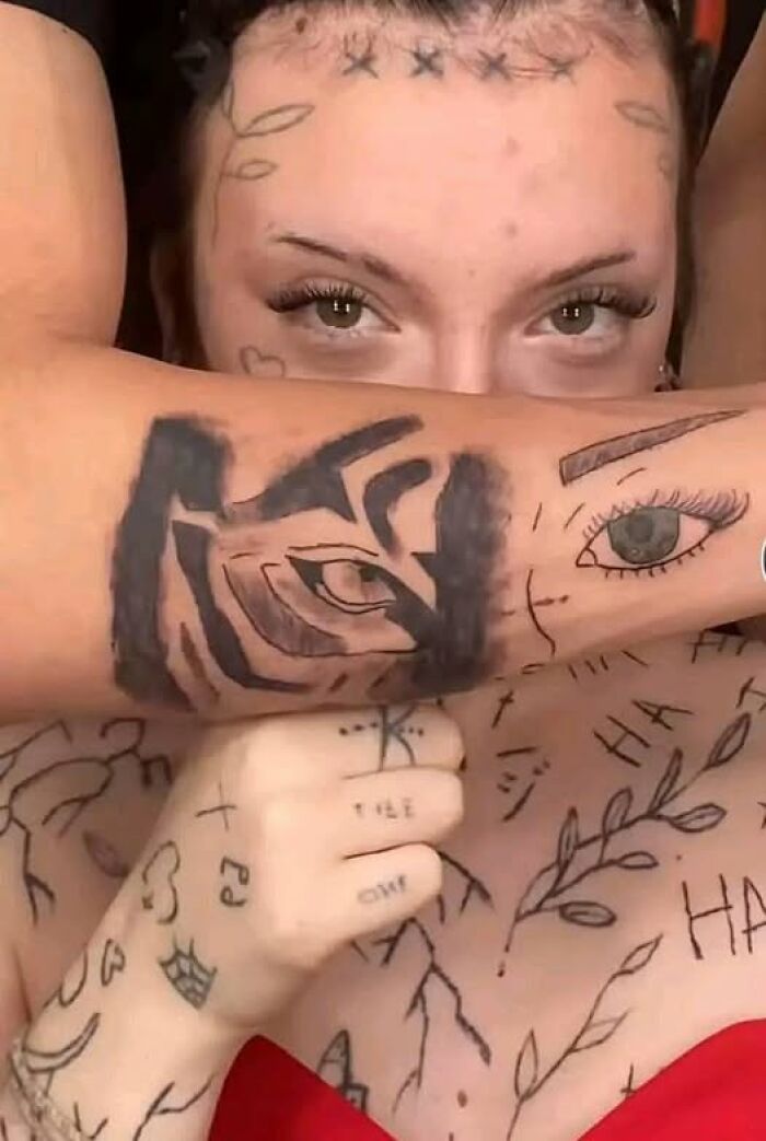 Person with multiple tattoos on face and arms, including abstract and eye designs, showcasing inked mistakes and cool tattoos.