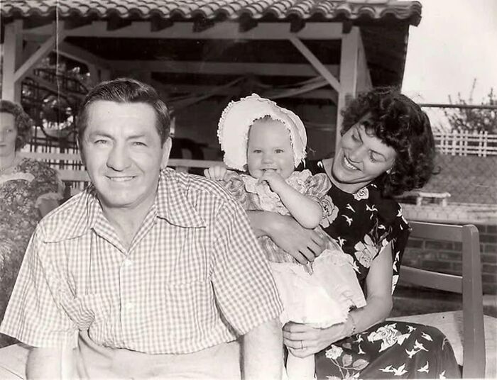 Vintage family portrait from antique historical photographs showing a smiling man, woman, and baby outdoors under a tiled roof.