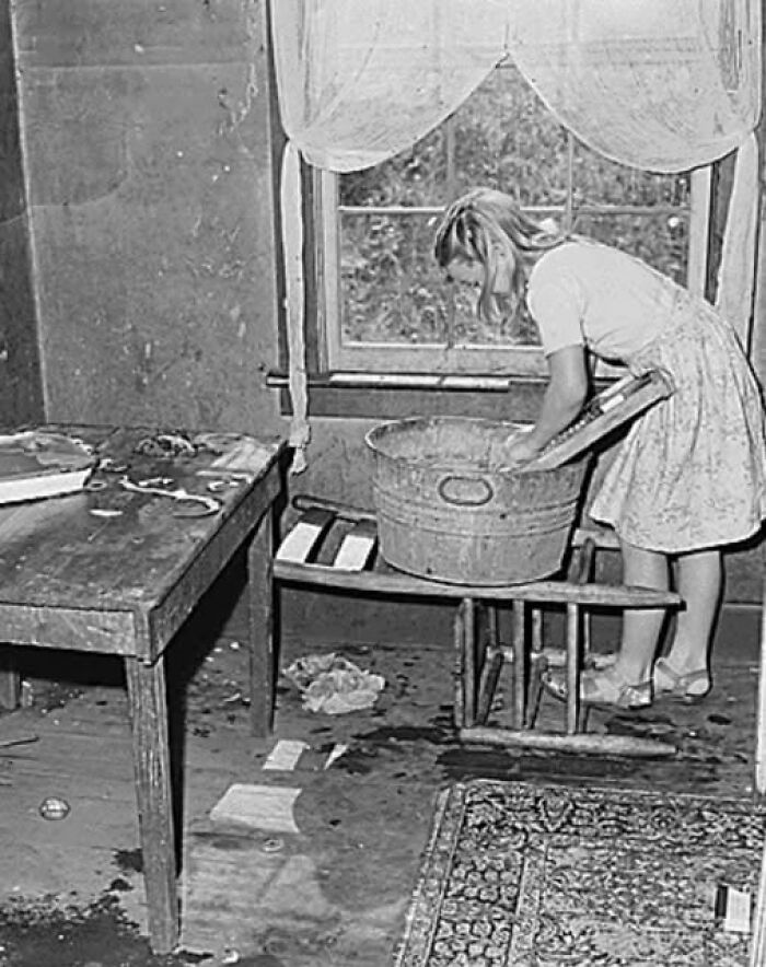Young girl washing clothes in a basin by the window in an antique historical photograph showing past daily life.