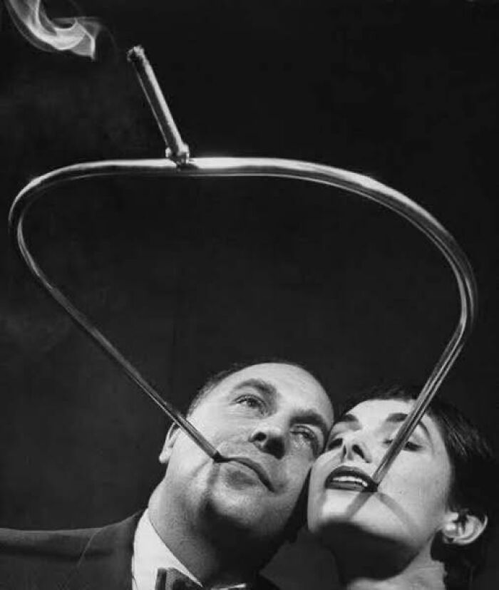 Man and woman in an antique historical photograph playing with a smoking pipe frame creating smoke patterns above them.