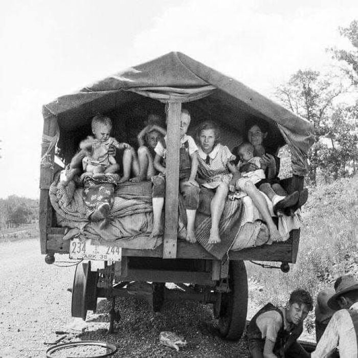 Family riding in the back of a covered truck on a rural road in an antique historical photograph.