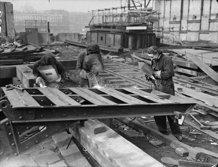 Women welding metal beams in an antique historical photograph showing early 20th-century industrial work.