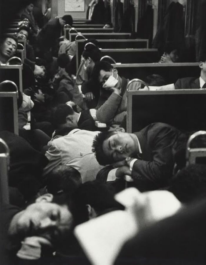 Crowded vintage train carriage with passengers sleeping and resting in an antique historical photograph depicting past daily life.