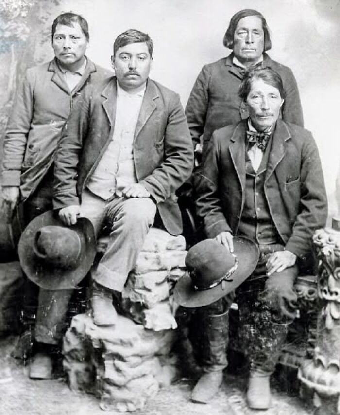 Four men in antique historical photographs wearing vintage suits and holding hats, sitting and standing in a studio setting.