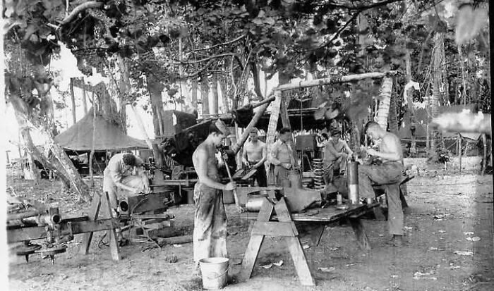 Group of men working with antique tools outdoors surrounded by trees in a historical photograph from the past.