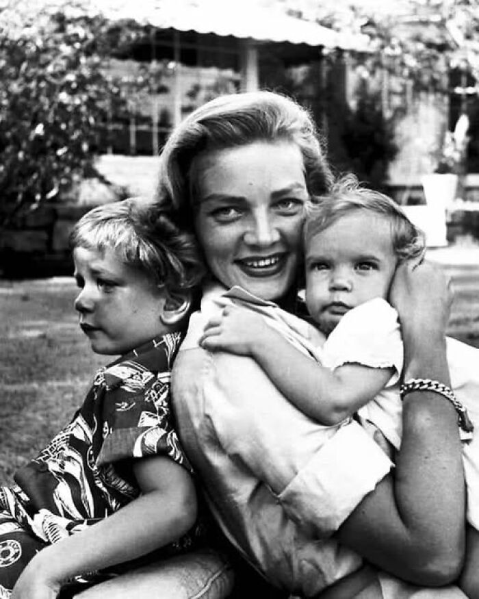 Black and white antique historical photograph of a smiling woman holding a child with another child beside her outdoors.