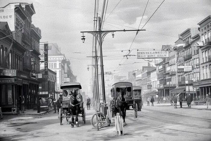 Antique historical photograph showing horse-drawn carriages on a busy early 20th century city street.