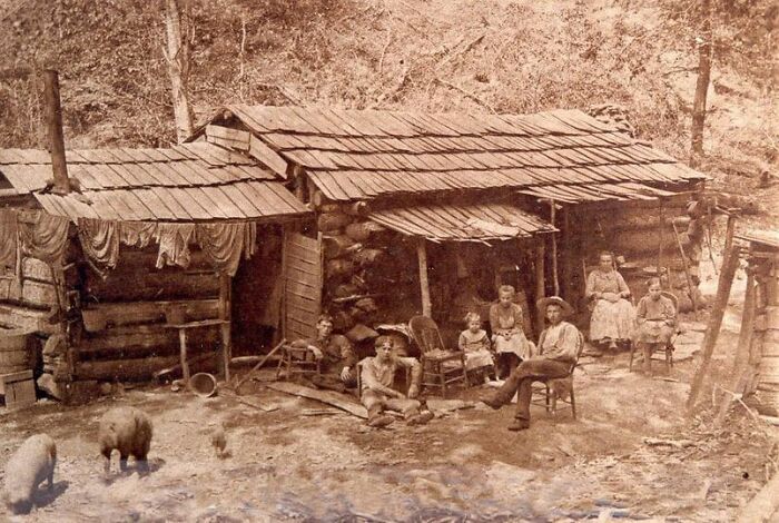 Family gathered outside a rustic log cabin in an antique historical photograph depicting life from the past.