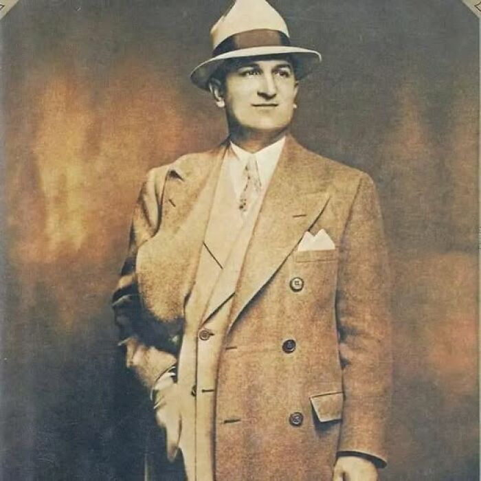 Vintage antique historical photograph of a man in a double-breasted coat and fedora hat posing confidently.