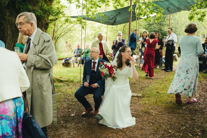 Couple sitting on a swing at an outdoor wedding reception surrounded by guests enjoying food and drinks.