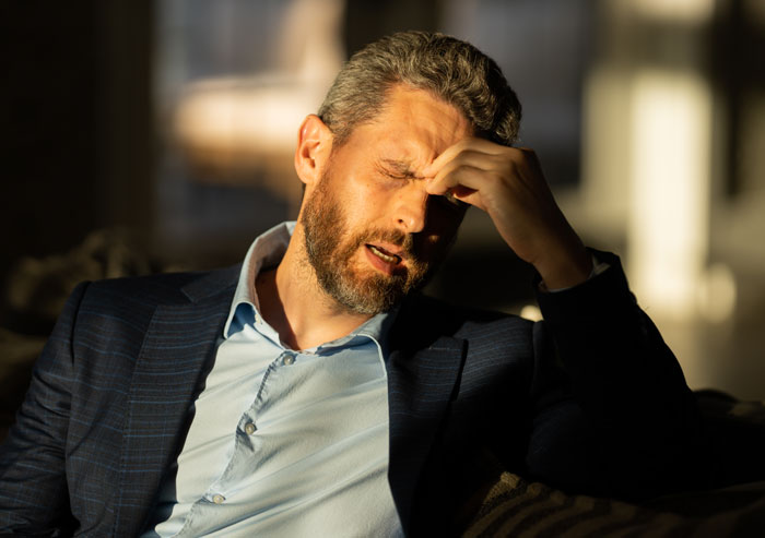 Man in a suit, stressed and rubbing forehead, depicting frustration over wedding photography gift turning into $3,000 bill.