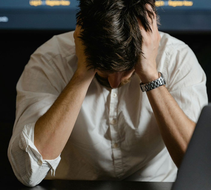 Frustrated man in white shirt holding his head, representing manager told staff not to fill empty shelves and sales issues.