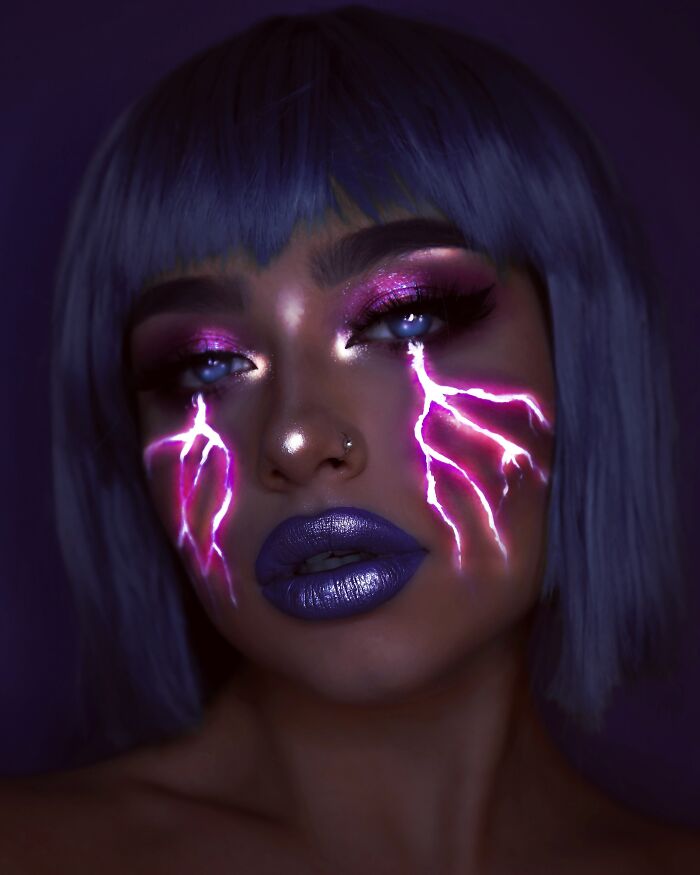 Creative makeup look featuring glowing purple lightning effects on cheeks with bold purple lips and shimmery eyeshadow.