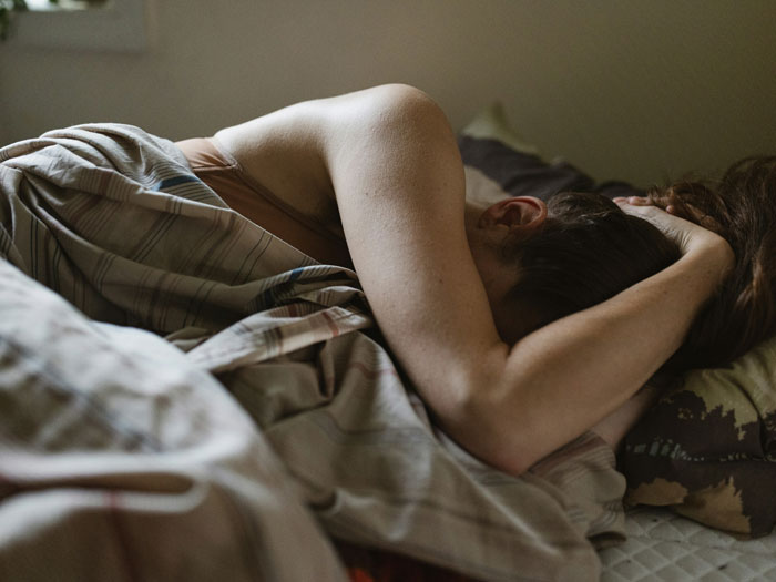 Person curled up in bed with head in hands, conveying emotion related to escaping from cults and personal struggle.