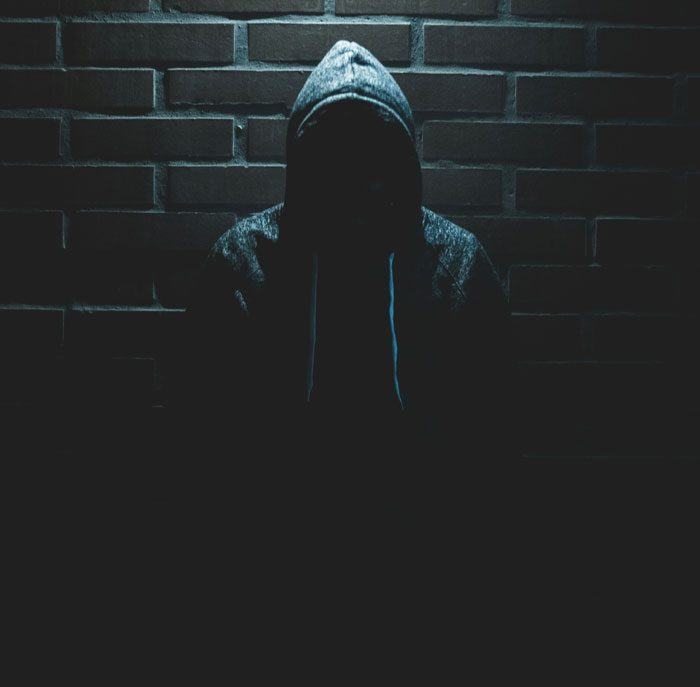 Person wearing a hooded jacket sitting alone against a dark brick wall, symbolizing lost friendship after 10+ years.
