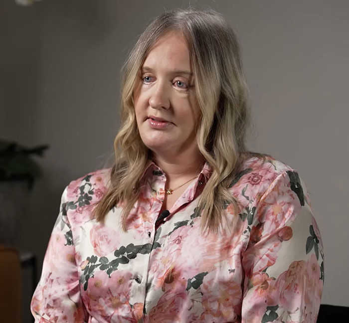 Woman sharing experience of plastic surgeon disfiguring her after seeking a refreshed look, wearing floral blouse indoors.