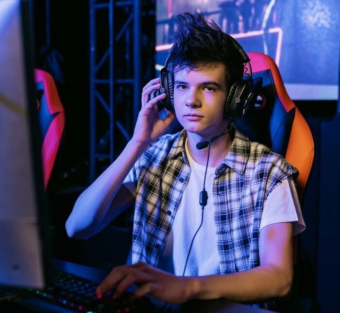Teen gamer wearing headset and using keyboard while seated in gaming chair, illustrating real-life cheat codes concept.