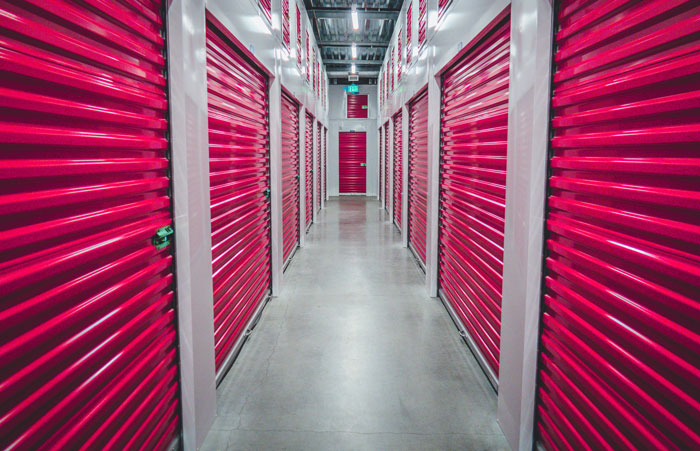 Indoor storage facility with red roll-up doors lining an empty corridor, illustrating ways people lose money saving.