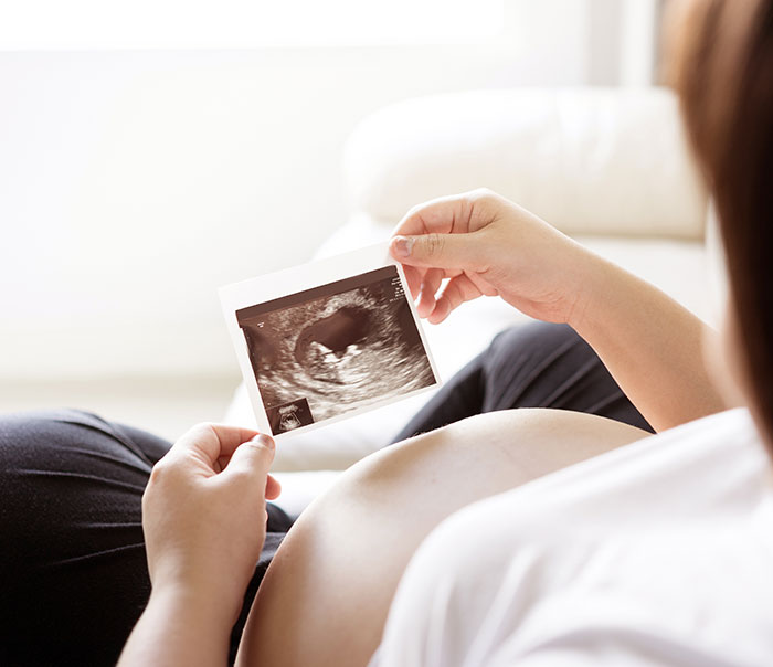 Pregnant woman holding ultrasound showing hand of God appearing after praying for baby's health.