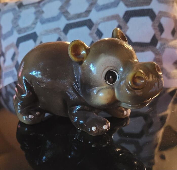 Glossy vintage hippo figurine thrifted find with large eyes and detailed features on reflective surface indoors.