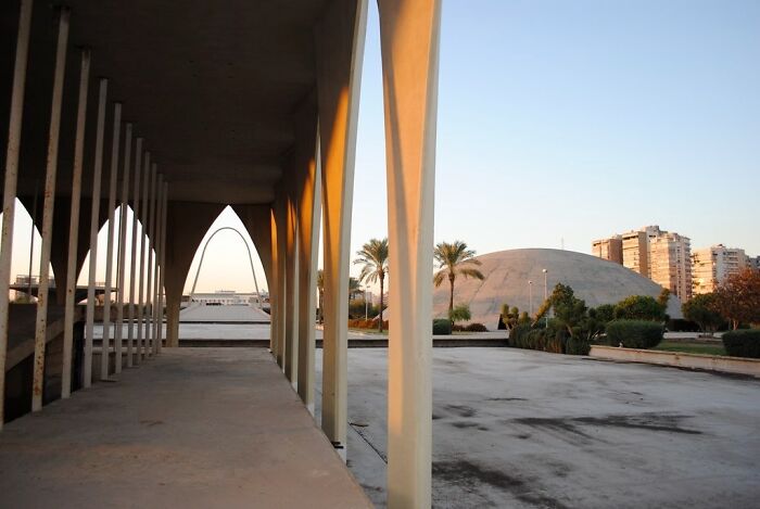 Modern UNESCO treasure featuring arched columns, palm trees, and a dome structure in an urban outdoor setting at sunset.