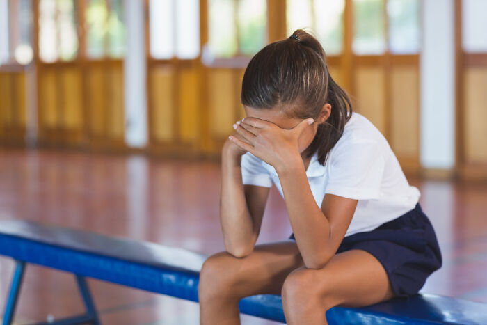 Young girl sitting on a bench covering her face, feeling emotional after hearing soul-crushing things from parents.