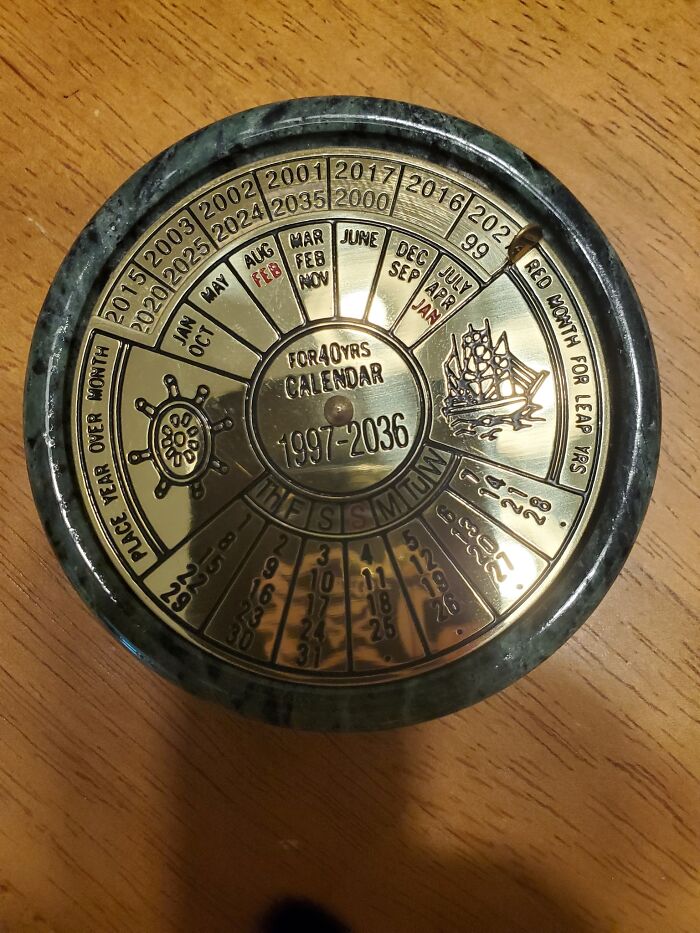 Circular vintage brass perpetual calendar from 1997-2036 thrifted find with intricate details on a wooden surface