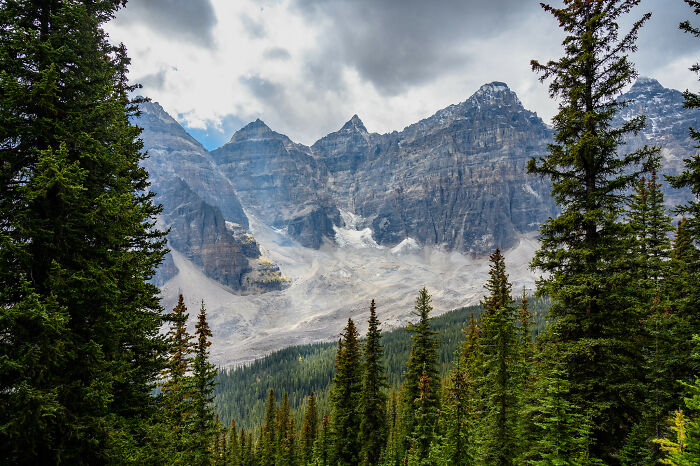 Mountain peaks rising above a dense forest under a cloudy sky, showcasing natural wonders that prove the world is full of magic.