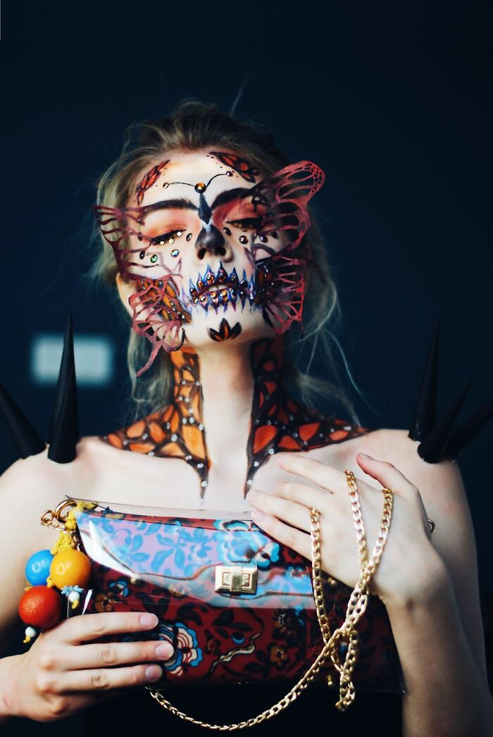 Woman with intricate butterfly-inspired makeup look holding a patterned purse with gold chain, showcasing creative makeup looks.