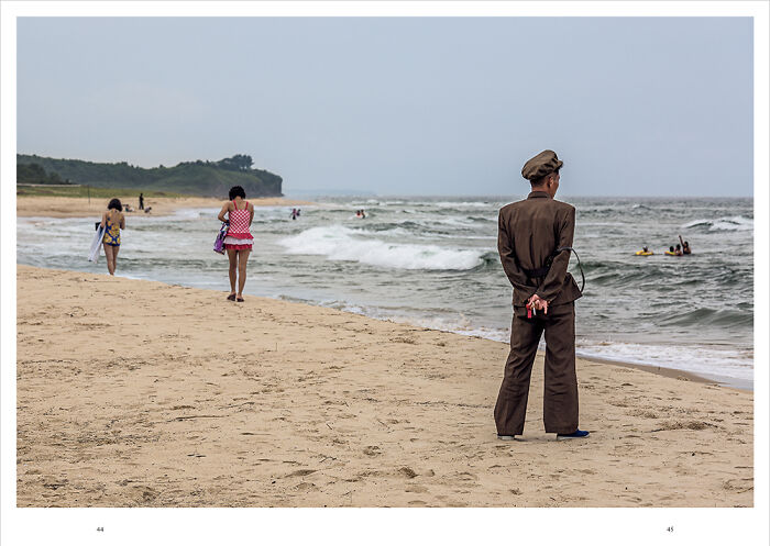 Man in uniform standing on beach while others walk near ocean waves, capturing essence of humanity in IPA 2024 Best Of Show.