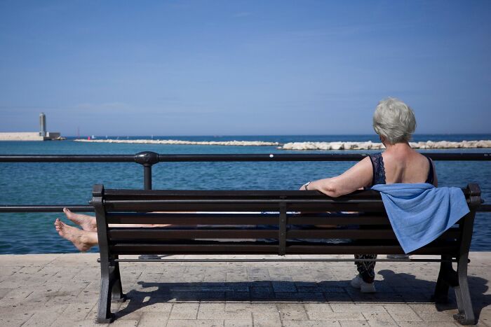 Elderly woman relaxing on a bench by the sea, embodying calm moments in pure street photography grant winning style.