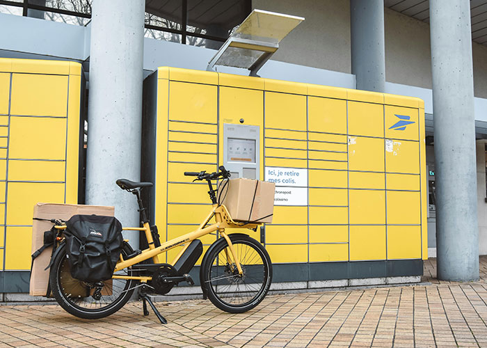 Yellow parcel locker with packages and a yellow bike in front, illustrating neighbor package theft and petty actions.