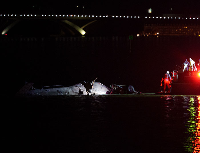 Wreckage of DC plane crash in water at night with rescue team searching the scene and emergency lights reflecting.