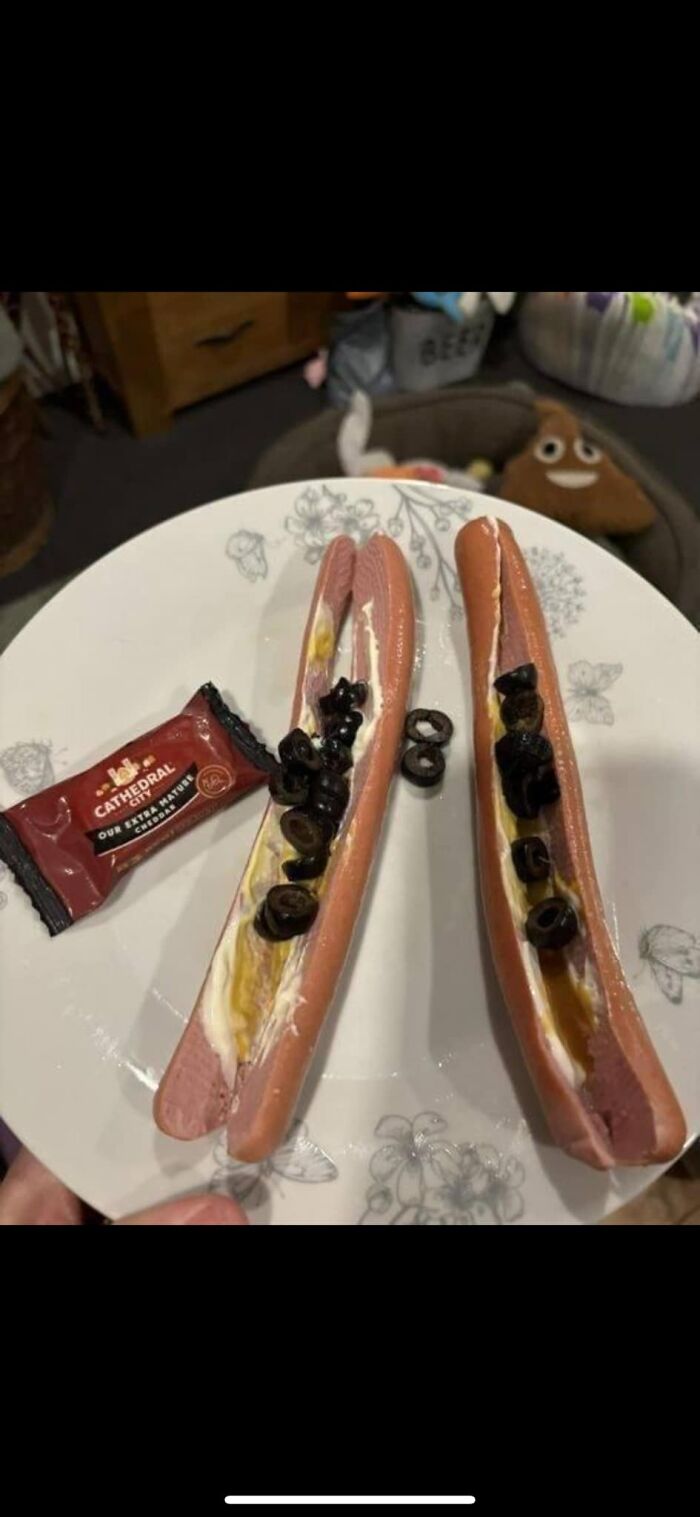 Two split hot dogs with mayonnaise and sliced black olives on a plate, showcasing cursed food pics trigger warning.