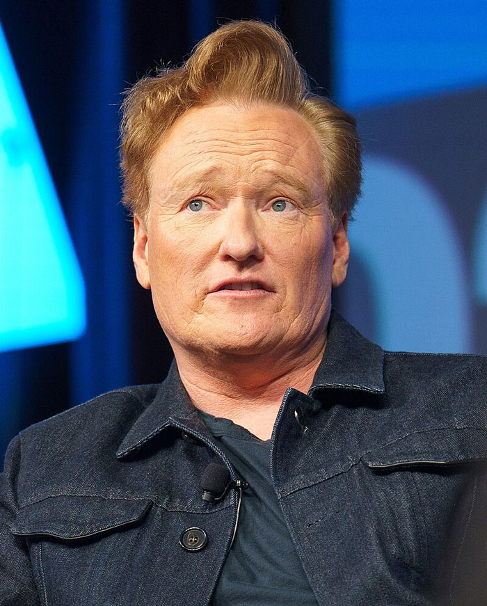 Comedian with reddish hair and denim jacket sharing a story about celebrity encounters that went really well or badly.