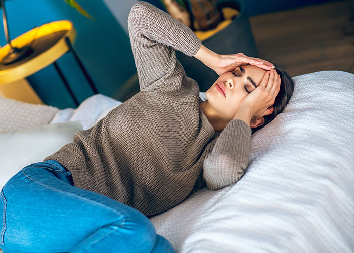 Woman lying on bed holding head in pain, illustrating common pathetic injuries shared by people.