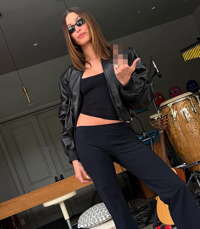 Woman in black leather jacket and sunglasses posing indoors amidst musical instruments with a pixelated hand gesture in focus.