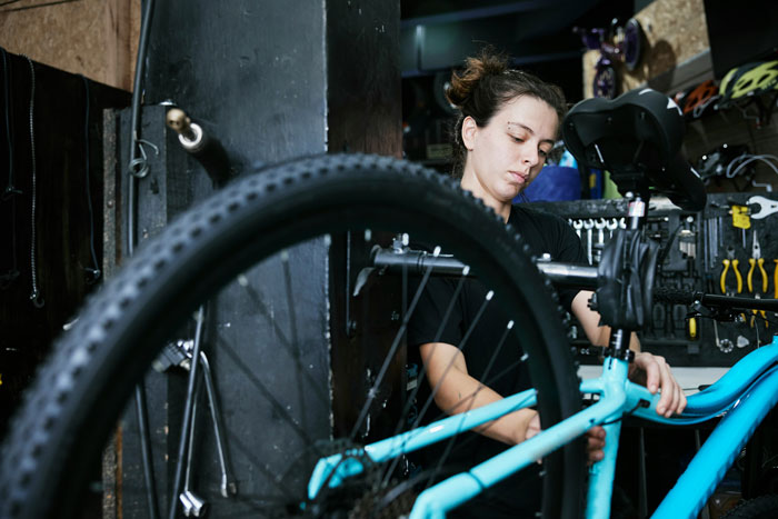 Woman repairing a bicycle in a workshop, illustrating ways people lose money while thinking they're saving.