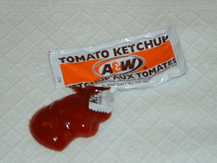 Ketchup packet squeezed open with ketchup spilled, illustrating a weird habit linked to being raised poor.