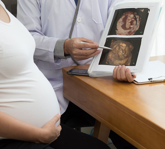 Pregnant woman with doctor examining ultrasound images showing hand of God appearing after praying for baby's health.