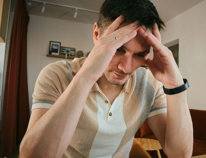 Man sitting indoors with hands on head, looking stressed about neighbor child digging and ruining lawn.