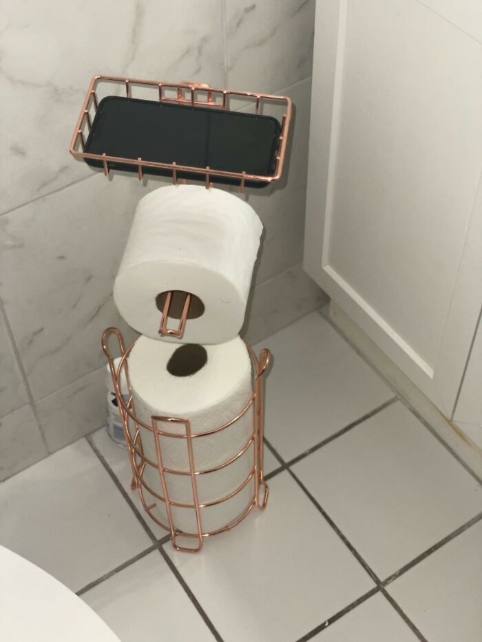 Organized bathroom corner with rose gold toilet paper holder and shelf for phone, illustrating ways to ditch the slob life.