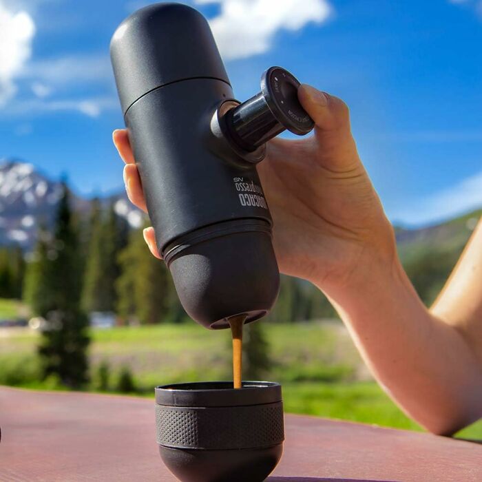 Hand holding a portable coffee maker pouring espresso outdoors with mountains and trees in the background, life threw lemons concept.