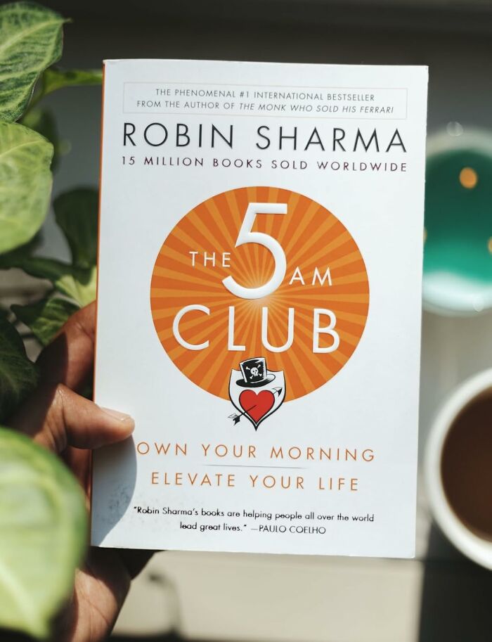 Hand holding The 5 AM Club book by Robin Sharma about owning your morning and becoming a morning person.