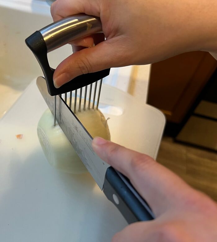 Hand using a smart kitchen gadget to evenly slice an onion with a knife and a slicing guide on a cutting board.