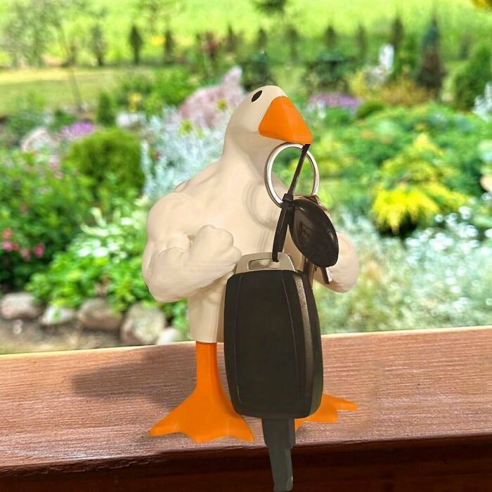 Weirdly wonderful key holder shaped like a muscular bird gripping car keys on a wooden surface with garden background