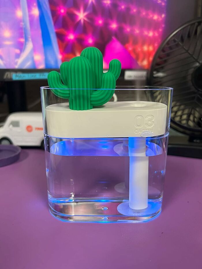 Cactus-shaped humidifier on a desk with office supplies and monitor background, adding charm to workspace.