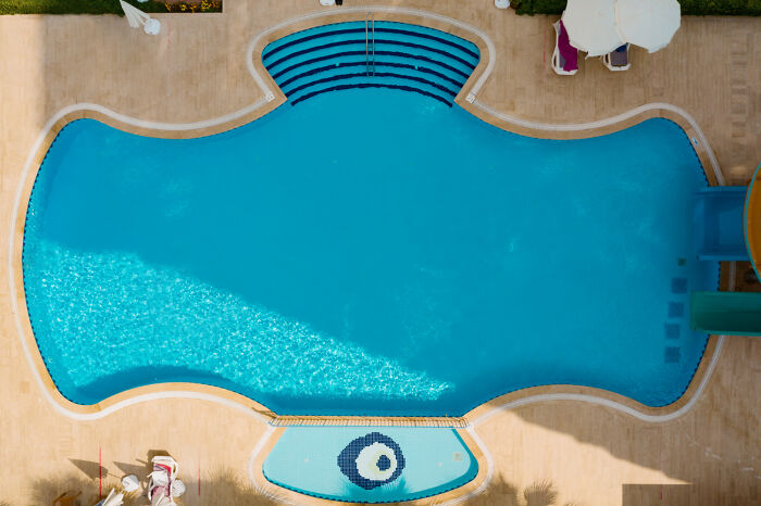 A top-down view of a clean outdoor pool with a surrounding deck and seating area on a sunny day