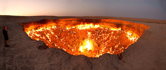 Panoramic view of a person standing near a large fiery crater, showcasing a rare natural phenomena at dusk.